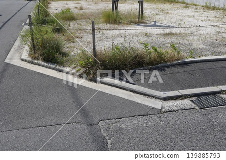 街角地塊。待租或待售土地圖片。雜草叢生,白色水泥地。房地產。 街角地塊。待租或待售土地圖片。雜草叢生,白色水泥地。房地產。 139885793