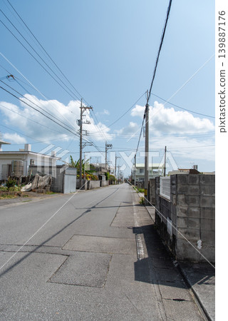 A long, straight street lined with utility poles, with the shadows of the power lines cast in the middle of the road, and no cars or people passing by. A long, straight street lined with utility poles, with the shadows of the power lines cast in the middle of the road, and no cars or people passing by. 139887176