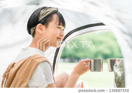 A child/girl lying down in a tent at a camp and drinking coffee (family camp) A child/girl lying down in a tent at a camp and drinking coffee (family camp) 139887358