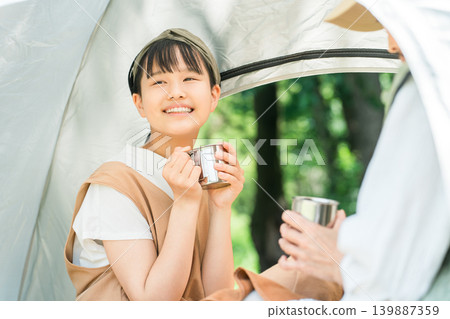 A child/girl lying down in a tent at a camp and drinking coffee (family camp) A child/girl lying down in a tent at a camp and drinking coffee (family camp) 139887359
