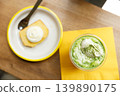 Cup of fresh matcha tea, green tea, topped with whipped cream and glazed lemen cake on wooden table. 139890175