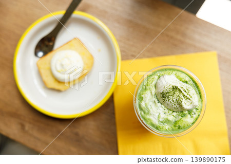 Cup of fresh matcha tea, green tea, topped with whipped cream and glazed lemen cake on wooden table. Cup of fresh matcha tea, green tea, topped with whipped cream and glazed lemen cake on wooden table. 139890175