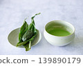 Cup of fresh matcha tea, green tea and Sasa dango, traditional Japanese confectionery wrapped in bamboo leaves, Sasa, on white table. 139890179