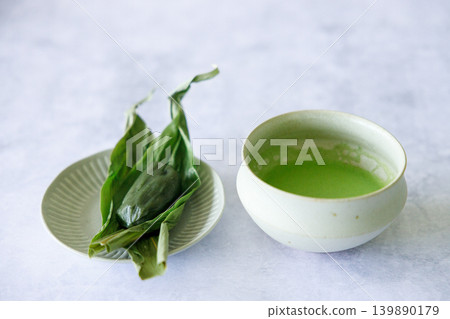 Cup of fresh matcha tea, green tea and Sasa dango, traditional Japanese confectionery wrapped in bamboo leaves, Sasa, on white table. 139890179
