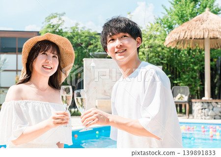 Couple toasting with champagne glasses by the pool at a resort hotel on vacation Couple toasting with champagne glasses by the pool at a resort hotel on vacation 139891833