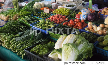 Market stall overflowing with fresh vegetables and herbs including cabbage, tomatoes, daikon, chili, onion, lime, green mango, Thai basil, cucumbers, eggplants, beans and greens 139892496