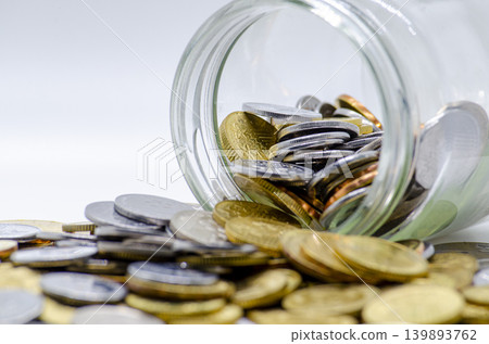 Coins spilling from a glass jar on a clean white background Coins spilling from a glass jar on a clean white background 139893762