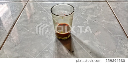 Empty glass cup with remaining drink on ceramic tile floor Empty glass cup with remaining drink on ceramic tile floor 139894680