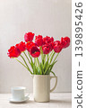 Bouquet of red tulip flowers in the white jug and cup of tea or coffee on a table against white background 139895426