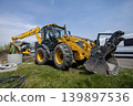 A yellow backhoe works at a construction site during the day. Another backhoe is visible in the background. The site has various construction materials. loader 139897536