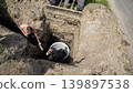 Two workers are digging a large hole in the ground. They are preparing to install a circular structure in a rural area under bright sunlight 139897538