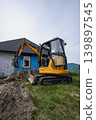 An excavator is digging near a house with blue walls while workers plan for an ongoing renovation project in the daytime 139897545