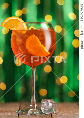 Refreshing aperol spritz cocktail in a festive glass on rustic wooden table with sparkling bokeh lights in vibrant green background, celebrating cheerful moment Refreshing aperol spritz cocktail in a festive glass on rustic wooden table with sparkling bokeh lights in vibrant green background, celebrating cheerful moment 139897685