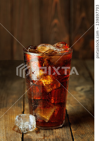 Refreshing sparkling cola with melting ice cubes in a glass creating condensation on rustic wooden background Refreshing sparkling cola with melting ice cubes in a glass creating condensation on rustic wooden background 139897703