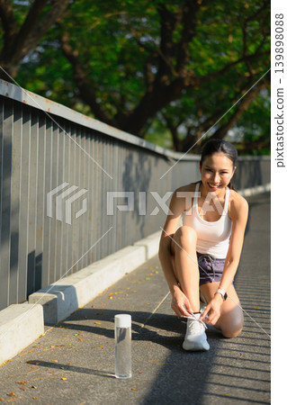 Runner woman tying laces on skywalk of park in urban city. Jogging girl exercise motivation health and fitness. Runner woman tying laces on skywalk of park in urban city. Jogging girl exercise motivation health and fitness. 139898088