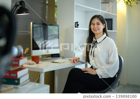 Smiling young Asian businesswoman sitting at her modern home office desk Smiling young Asian businesswoman sitting at her modern home office desk 139898100