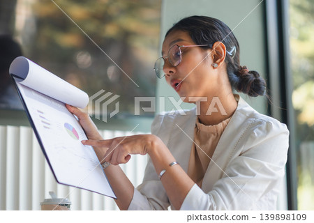 Side view businesswoman pointing to business report charts in office, explaining financial data, marketing analysis, strategy discussion, and confident professional presentation for team meeting. Side view businesswoman pointing to business report charts in office, explaining financial data, marketing analysis, strategy discussion, and confident professional presentation for team meeting. 139898109
