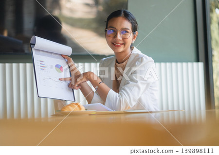 Smiling businesswoman in white blazer pointing to business report charts at office table, presenting financial data, marketing performance, growth strategy, and corporate teamwork success. Smiling businesswoman in white blazer pointing to business report charts at office table, presenting financial data, marketing performance, growth strategy, and corporate teamwork success. 139898111