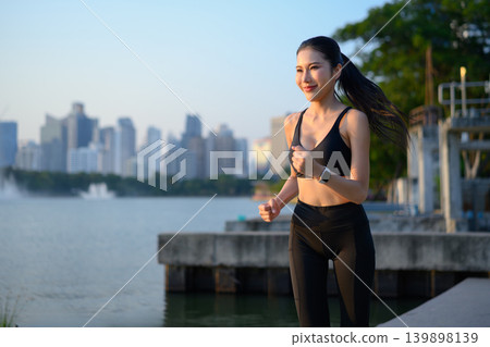 Fit woman jogging by lake with city skyline at sunrise Fit woman jogging by lake with city skyline at sunrise 139898139
