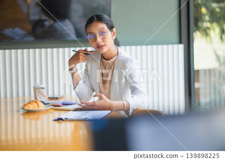 Professional businesswoman pointing to notes at an office table with pen, coffee, croissant, and paperwork, presenting planning details, business tasks, collaboration, and productive meeting workflow. Professional businesswoman pointing to notes at an office table with pen, coffee, croissant, and paperwork, presenting planning details, business tasks, collaboration, and productive meeting workflow. 139898225
