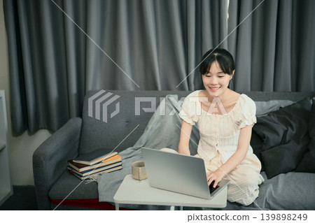 Young woman smiling while working on laptop indoors Young woman smiling while working on laptop indoors 139898249