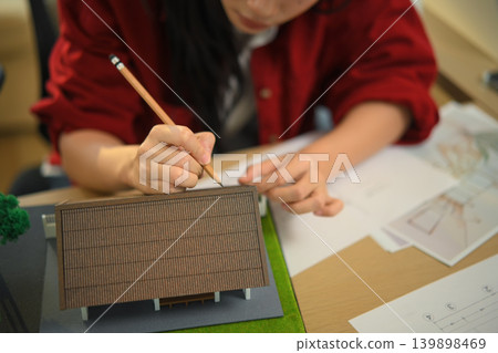 Closeup Female architect examining house model at office desk Closeup Female architect examining house model at office desk 139898469