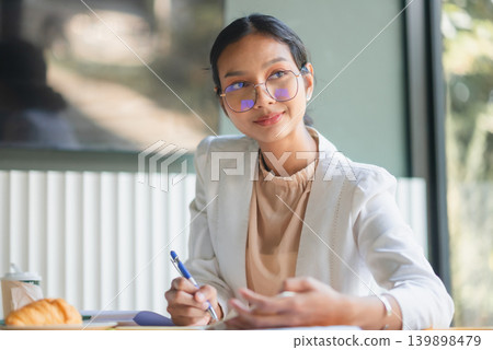Businesswoman explaining ideas with pen while sitting at office table with notes, coffee, and croissant, showing communication, strategy discussion, consulting, and productive meeting planning. 139898479