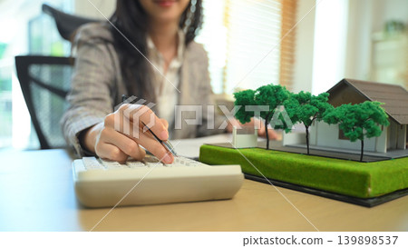 Real estate professional calculating property costs at desk, Close up of businesswoman calculating housing expenses. Real estate professional calculating property costs at desk, Close up of businesswoman calculating housing expenses. 139898537