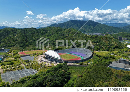 An aerial photograph overlooking Hiroshima Wide Area Park Athletics Stadium and the surrounding green mountains. An aerial photograph overlooking Hiroshima Wide Area Park Athletics Stadium and the surrounding green mountains. 139898566