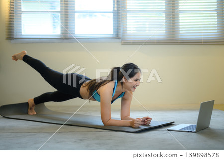 Woman doing plank workout while following laptop, home fitness and online training concept Woman doing plank workout while following laptop, home fitness and online training concept 139898578