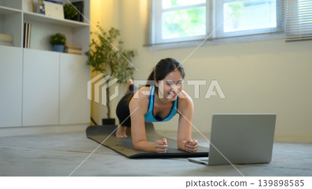 Woman doing plank workout while following laptop, home fitness and online training concept Woman doing plank workout while following laptop, home fitness and online training concept 139898585