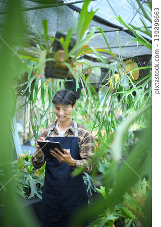 Gardener using tablet to check staghorn fern in greenhouse Gardener using tablet to check staghorn fern in greenhouse 139898663
