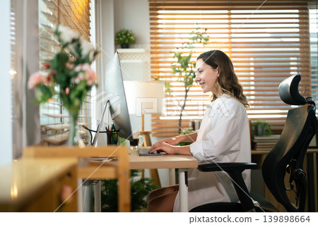 Smiling remote worker with computer at desk in bright home workspace 139898664