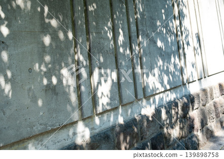 Sunlight filtering through trees onto a concrete wall creates a tranquil scene of light and shadow. Sunlight filtering through trees onto a concrete wall creates a tranquil scene of light and shadow. 139898758