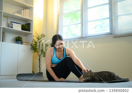 Woman resting after workout on yoga mat with cat, cozy home lifestyle and wellness moment Woman resting after workout on yoga mat with cat, cozy home lifestyle and wellness moment 139898802