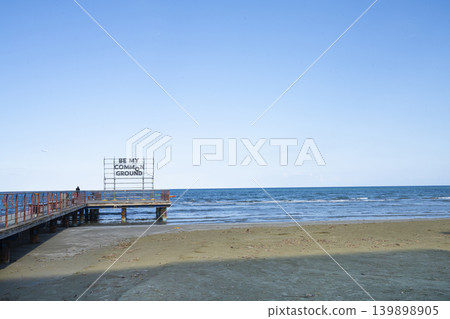 A person stands on a pier at the beach next to a sign that reads "BE MY COMMON GROUND" in Larlaka, Cyprus A person stands on a pier at the beach next to a sign that reads "BE MY COMMON GROUND" in Larlaka, Cyprus 139898905