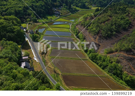 An aerial photograph overlooking rice paddies and farmland spread across a valley in the foothills of a rural mountain village. An aerial photograph overlooking rice paddies and farmland spread across a valley in the foothills of a rural mountain village. 139899219