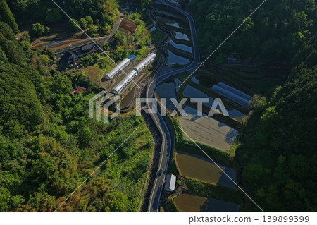 An aerial photograph overlooking the terraced rice fields and winding farm roads of Takahashi City, Okayama Prefecture. An aerial photograph overlooking the terraced rice fields and winding farm roads of Takahashi City, Okayama Prefecture. 139899399