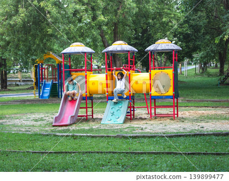 Two young Asian girls having fun playing on a colorful slide structure at the outdoor playground. Two young Asian girls having fun playing on a colorful slide structure at the outdoor playground. 139899477