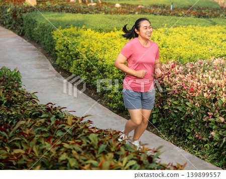 Active Asian woman brisk walking and exercising on a pathway in the public park. Active Asian woman brisk walking and exercising on a pathway in the public park. 139899557