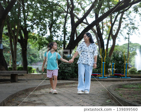 Happy Asian mother holding hands with her young daughter walking together after school. Happy Asian mother holding hands with her young daughter walking together after school. 139899560