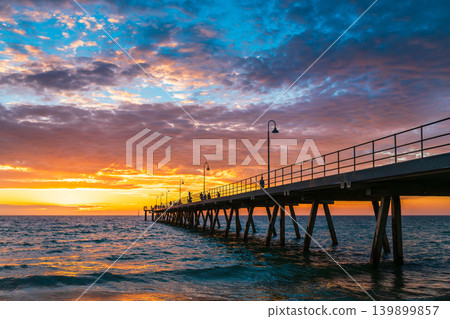 Sunset over Glenelg Beach Jetty with evening crowd of people strolling along 139899857