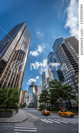 New york, usa august 19,2024. New york city streetscape featuring towering skyscrapers against a blue sky, with modern yellow taxis driving on the road 139900094