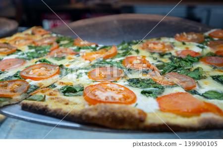 New york, usa august 19,2024. New york style thin crust pizza topped with fresh spinach, melted mozzarella and sliced tomatoes, hot and ready to serve New york, usa august 19,2024. New york style thin crust pizza topped with fresh spinach, melted mozzarella and sliced tomatoes, hot and ready to serve 139900105