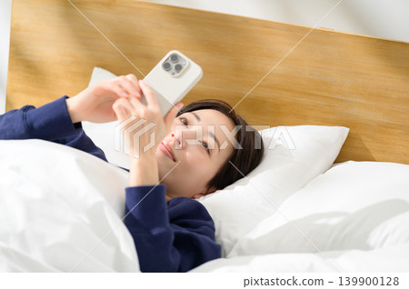 A Japanese woman operating a smartphone in bed A Japanese woman operating a smartphone in bed 139900128