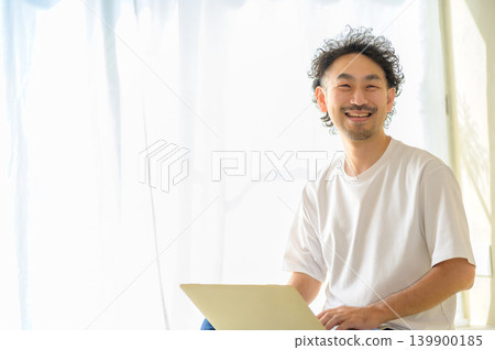 一位微笑的日本男子在家中使用筆記型電腦。 一位微笑的日本男子在家中使用筆記型電腦。 139900185