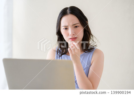 A Japanese woman pondering while looking at her laptop. A Japanese woman pondering while looking at her laptop. 139900194