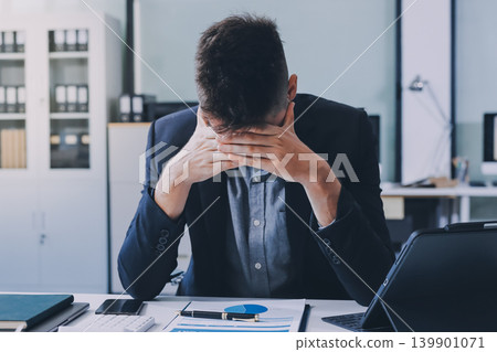 Tired worker. A tired businessman works in the evening. A man in office clothes is holding his temples. Problems in business. The businessman is trying to solve the problems that have arisen. Tired worker. A tired businessman works in the evening. A man in office clothes is holding his temples. Problems in business. The businessman is trying to solve the problems that have arisen. 139901071