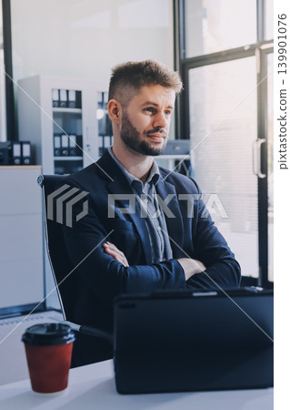 Smiling businessman in suit works on laptop in bright modern office Smiling businessman in suit works on laptop in bright modern office 139901076
