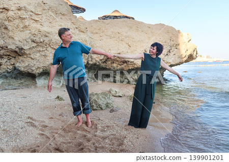 A husband and wife are joking on the beach while holding hands 139901201